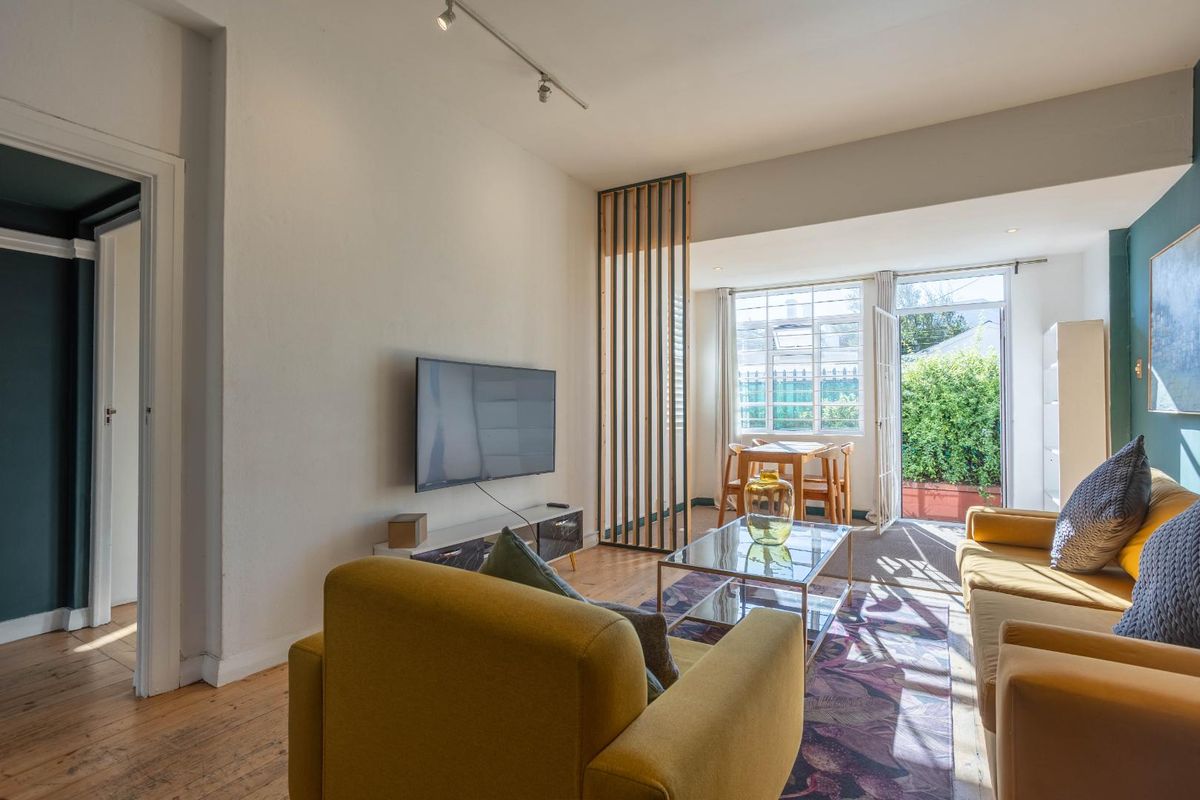 Bright living room featuring timber flooring, a decorative timber slat room divider, and direct access to an outdoor patio area through a glass door.