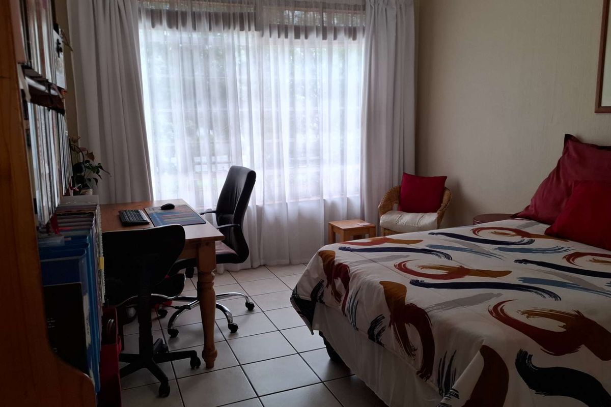 A bedroom featuring tiled flooring and large windows with curtains, providing natural light and access to the exterior.