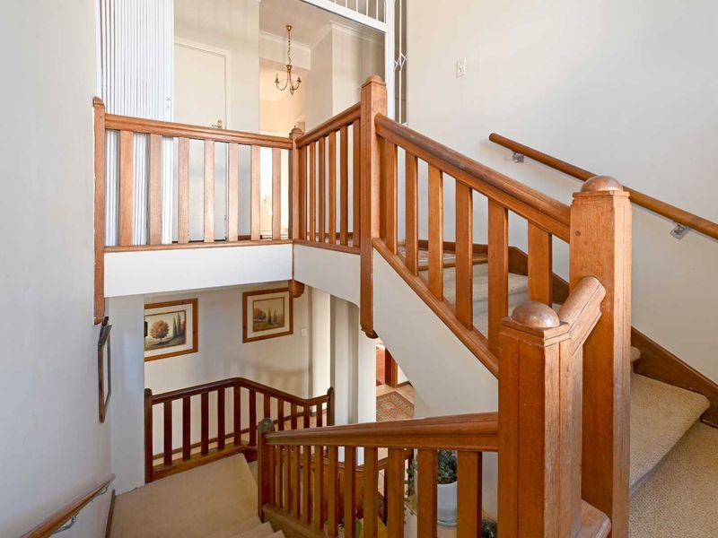 A bright, multi-level hallway featuring a classic timber staircase with matching balustrades and carpeted steps, connecting different levels of the home.