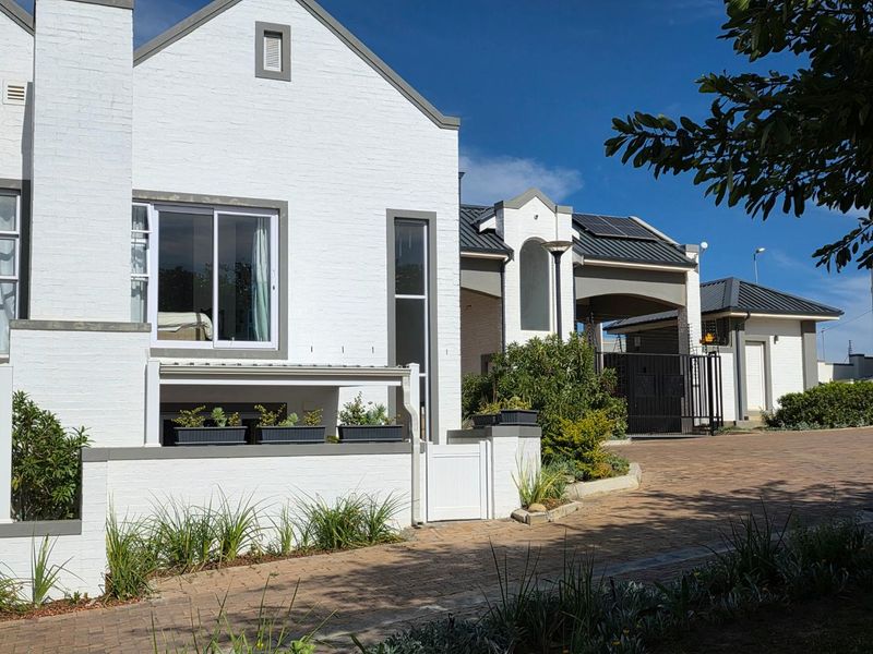 A well-maintained townhouse exterior featuring a white painted brick facade, metal roofing, and paved driveway leading to a secure gated entrance.