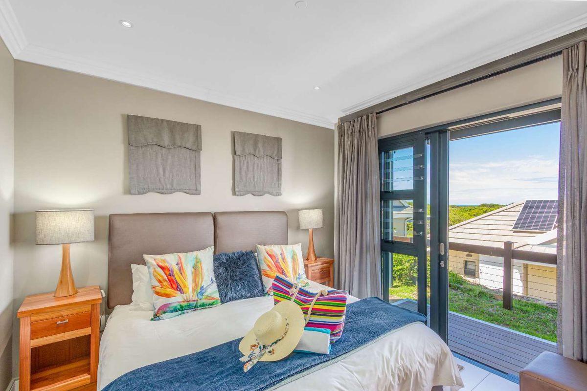 A bright bedroom featuring neutral walls, recessed lighting, and sliding glass doors that open onto a private balcony with scenic views.