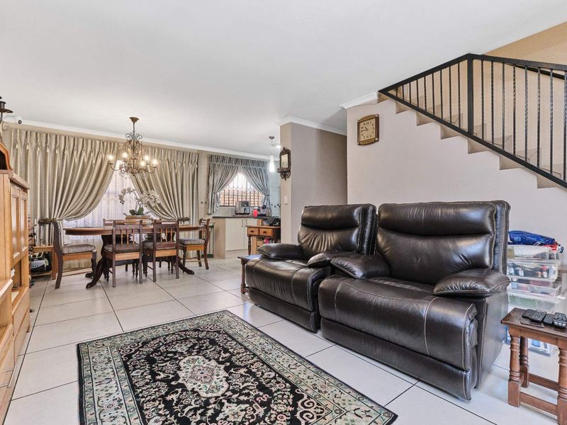 Open-plan living and dining area featuring tiled flooring and a staircase with a metal railing, leading to a compact kitchen space.