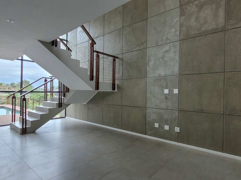 Spacious living area featuring a modern staircase, striking concrete feature wall, large windows, and direct access to an outdoor pool area.