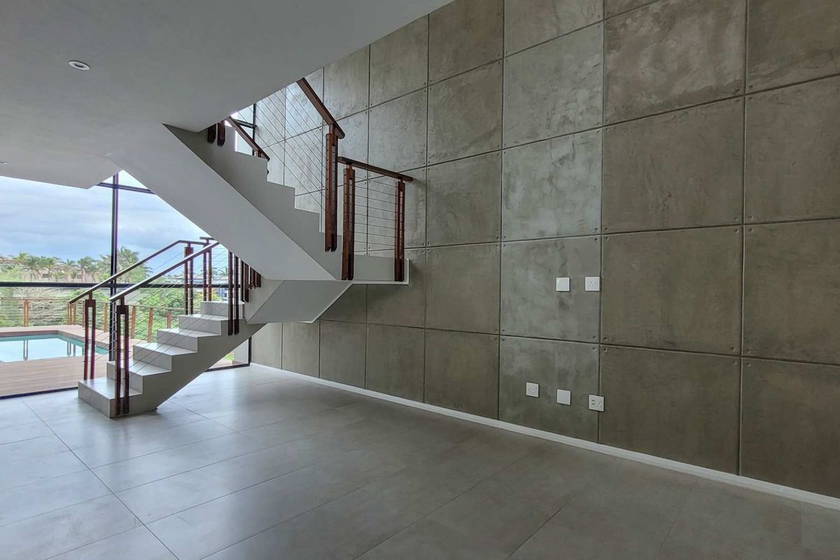 Spacious living area featuring a modern staircase, striking concrete feature wall, large windows, and direct access to an outdoor pool area.