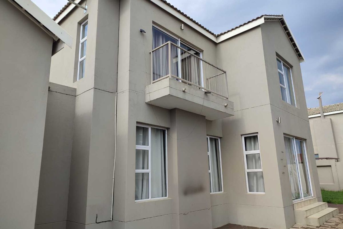 Rear exterior view of a two-story residential property featuring a balcony, paved patio area, and modern window frames.