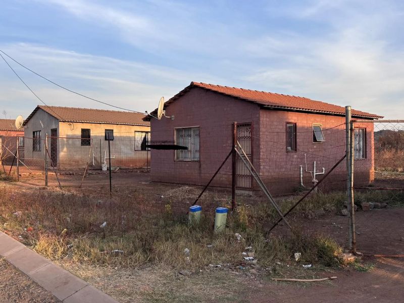 A view of a detached residential house featuring a tiled roof, security gate, and wire mesh perimeter fencing in a suburban setting.