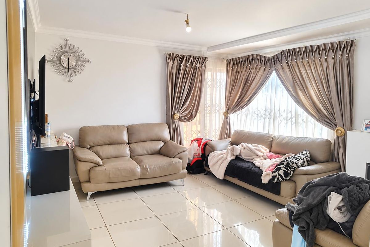 A bright and spacious living room featuring polished tiled flooring, decorative cornicing, and large windows fitted with security gates.