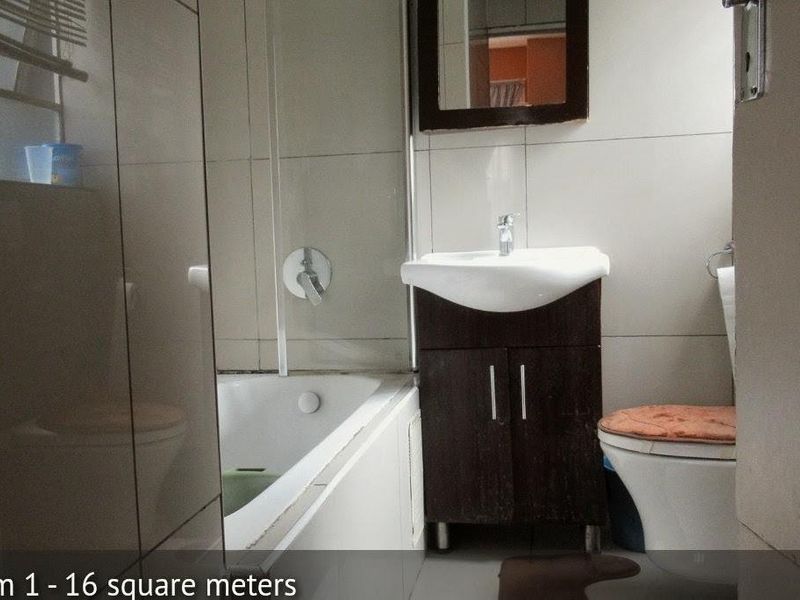 A functional bathroom featuring a bathtub, vanity cabinet with basin, and toilet, finished with neutral wall tiles.