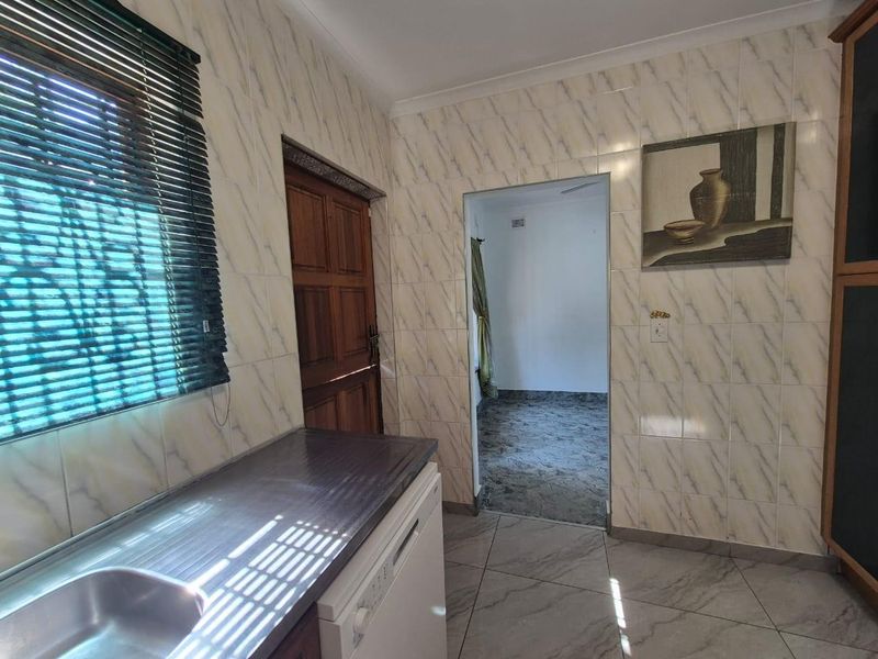 A functional kitchen area featuring tiled walls, tiled flooring, a stainless steel sink, and a laminate countertop with access to an adjacent room.