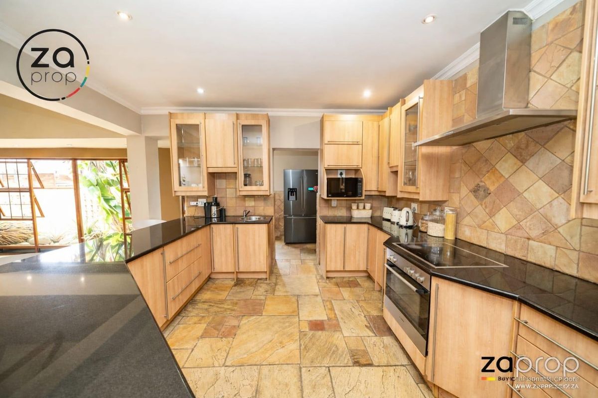 A spacious kitchen featuring light wood cabinetry, black granite countertops, stone tile flooring, and integrated stainless steel appliances including an oven and extractor fan.