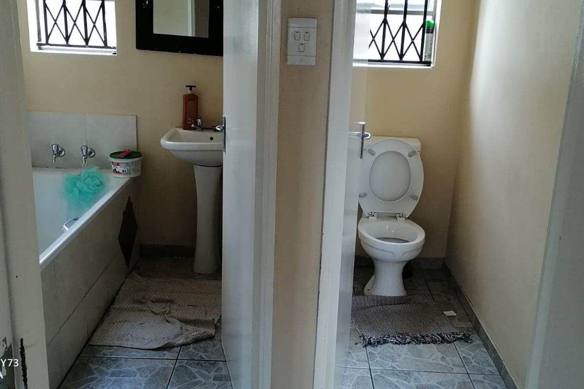 A split-view bathroom featuring a separate bathtub and pedestal basin area alongside a private toilet cubicle with tiled flooring and security bars.