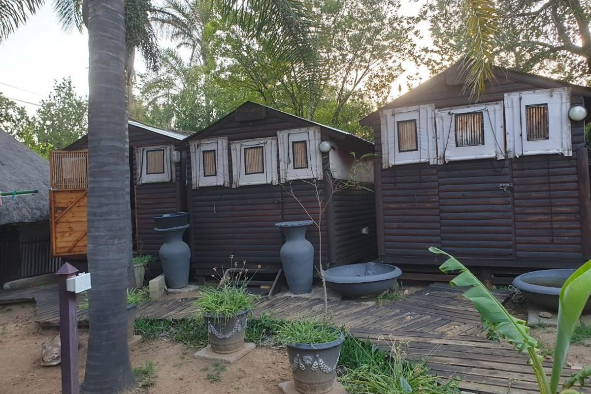 Exterior view of timber cottage structures featuring wooden log-style cladding and integrated window shutters set within a garden environment.