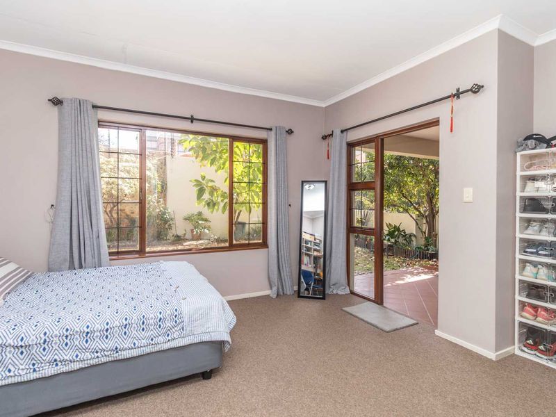 A bedroom featuring carpeted flooring, timber-framed windows, and a sliding door providing direct access to an outdoor patio area.
