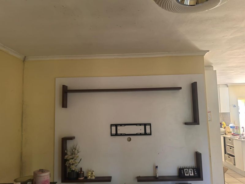 A living room wall featuring a built-in shelving unit and TV mounting bracket, showing signs of wear on the walls and ceiling.