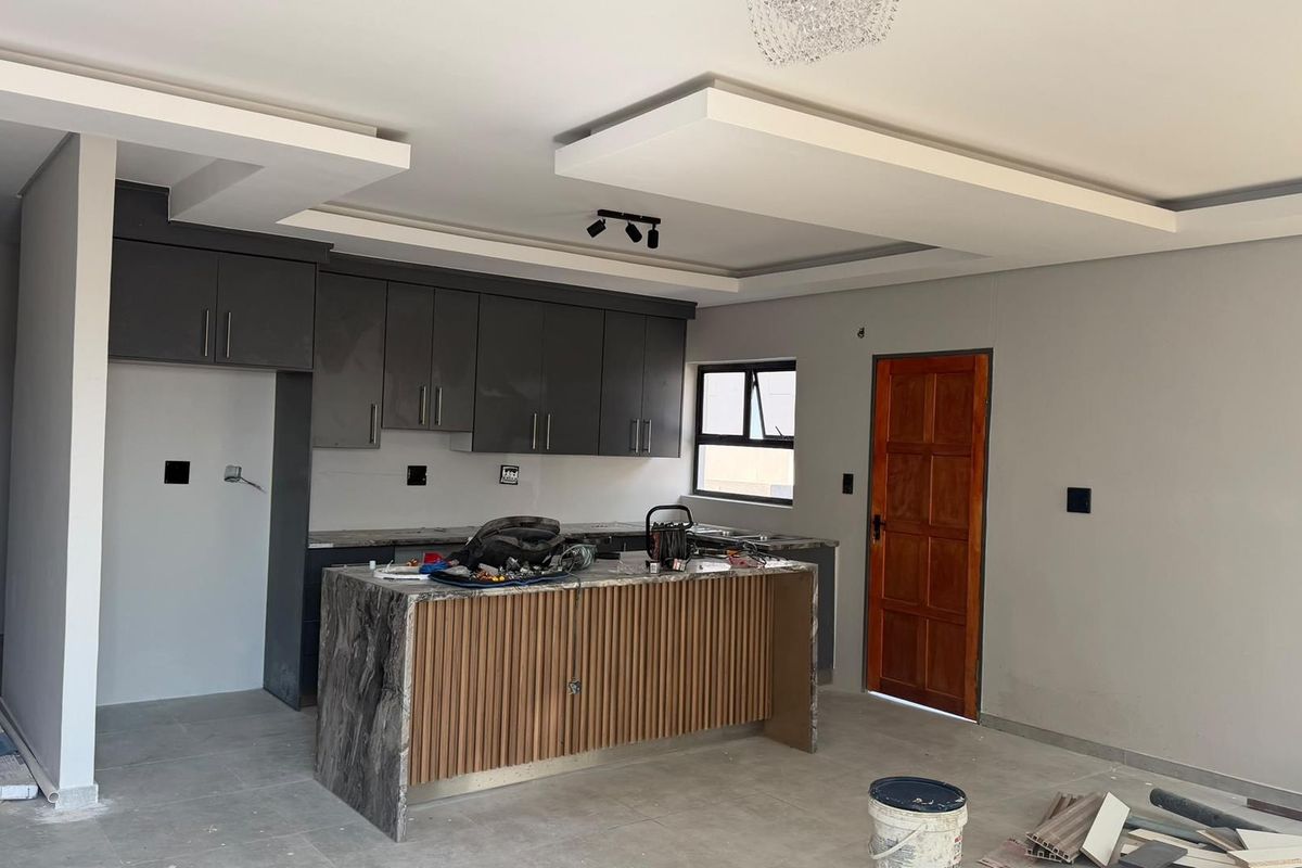 Modern kitchen featuring dark grey cabinetry, a stone-topped island with slatted wood detailing, and a contemporary dropped ceiling design, currently in final stages of completion.