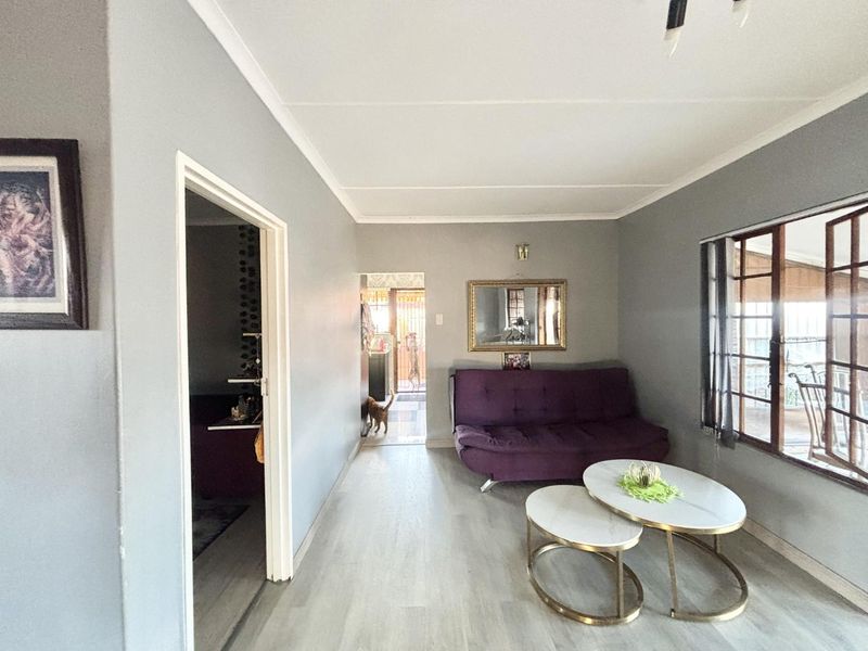 A living room featuring light-toned laminate flooring, neutral grey walls, and timber-framed windows, providing a functional and well-lit space.