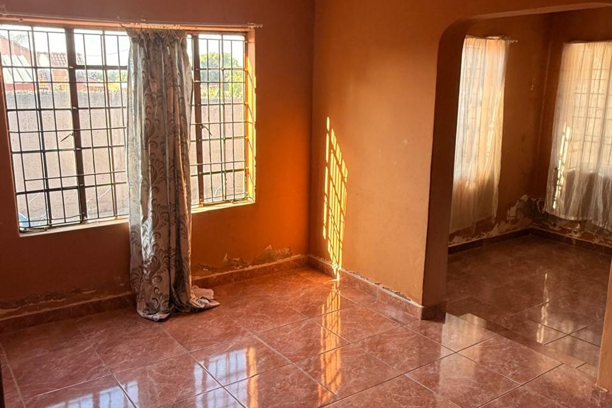 An empty living area featuring tiled flooring, security bars on windows, and an arched transition to an adjacent space, showing signs of wear.