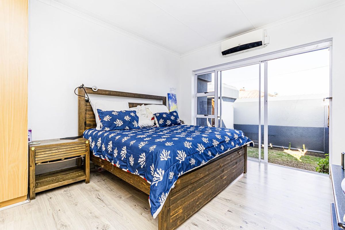 A bright bedroom featuring light laminate flooring, a built-in wardrobe, and a split-system air conditioner, with direct access to an outdoor area via sliding doors.
