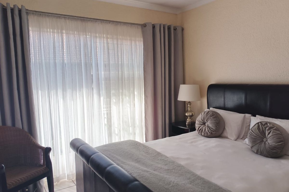 A well-lit bedroom featuring tiled flooring and large sliding glass doors with curtain tracks, providing natural light and access to the exterior.