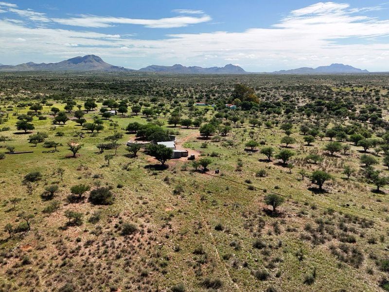 An aerial view of a vast farm property featuring open grazing land, scattered indigenous trees, and distant mountain vistas.