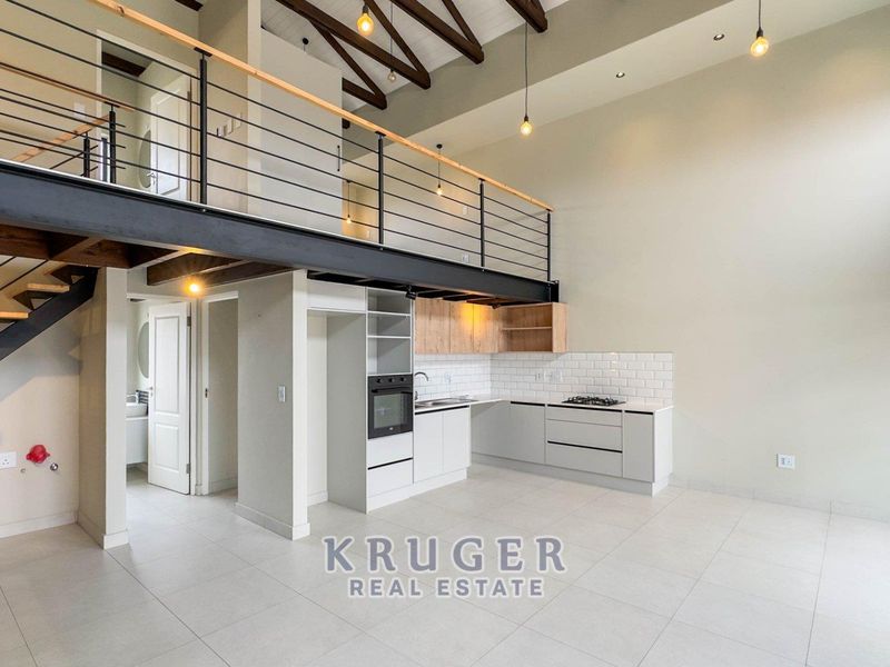 Modern open-plan kitchen and living area featuring a mezzanine level, exposed timber beams, sleek cabinetry, and high-quality tiled flooring throughout.