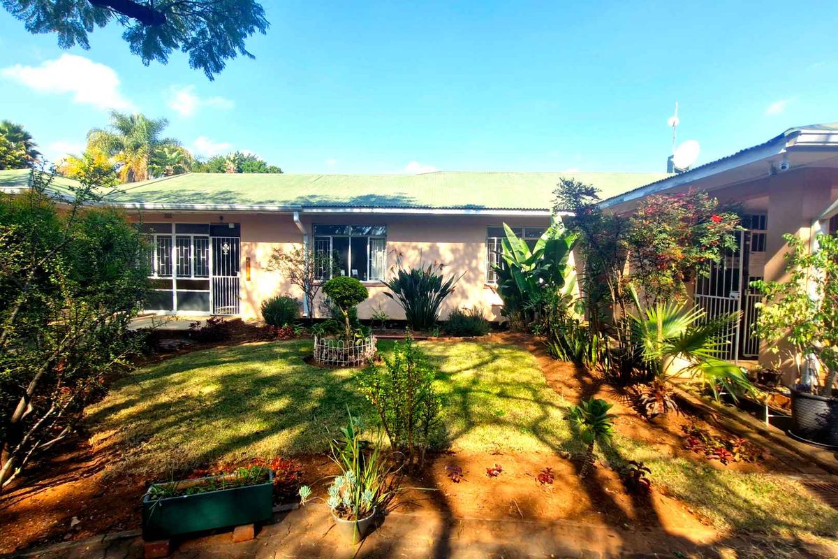 A rear view of the house featuring a landscaped garden, lawn area, and access to the building's rear facade with security gates.