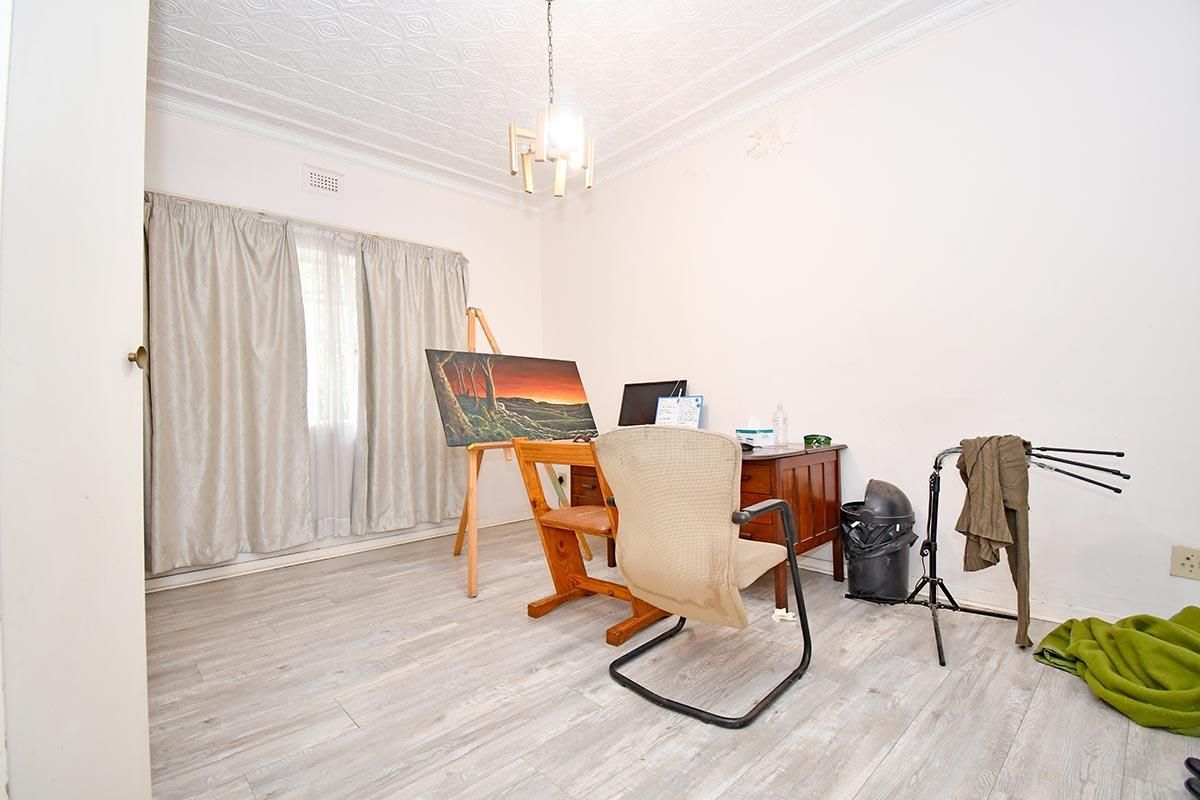 A functional bedroom or home office space featuring light-toned wood-look flooring, decorative pressed metal ceiling, and a window with curtain treatments.