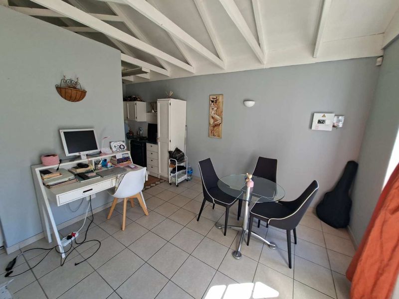 Open-plan living area featuring exposed timber rafters, neutral wall finishes, and ceramic floor tiling, providing a versatile space for dining and home office use.