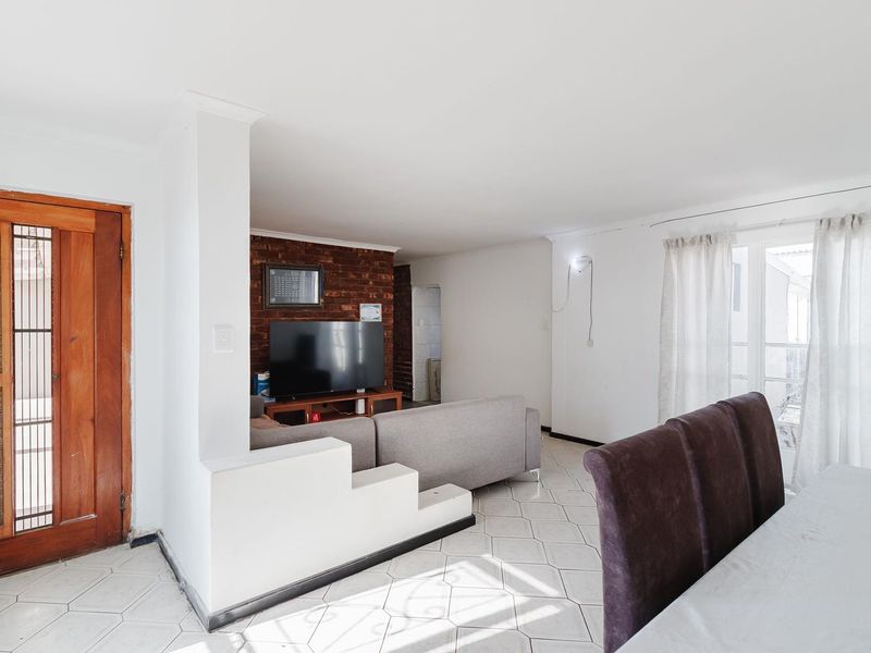 Open-plan living and dining area featuring tiled flooring, an exposed brick feature wall, and direct access to the exterior via a sliding glass door.