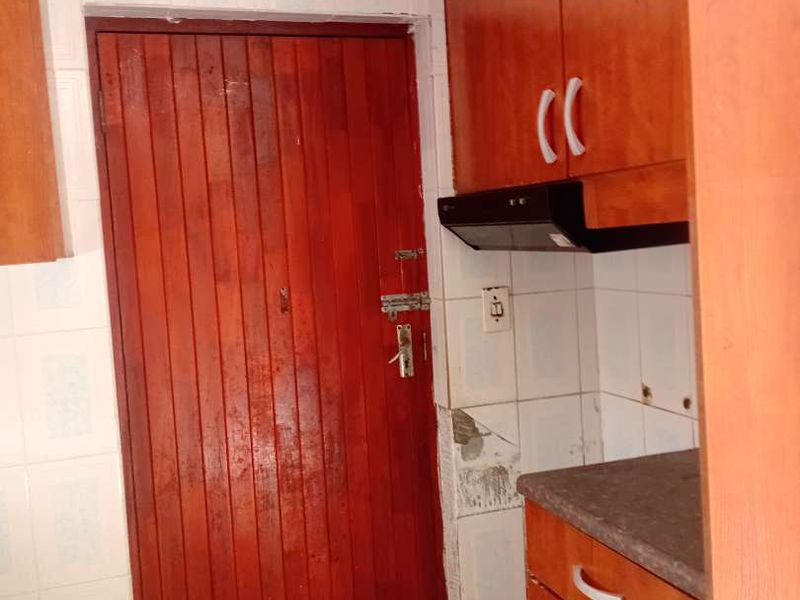 A compact kitchen featuring wooden cabinetry, a built-in extractor fan, and tiled splashbacks, requiring some maintenance to the wall tiles and door finish.