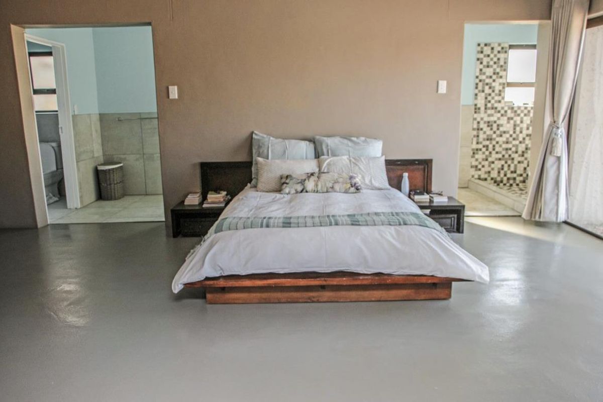 Spacious bedroom featuring polished concrete floors, built-in bedside tables, and direct access to an en-suite bathroom with a tiled shower.