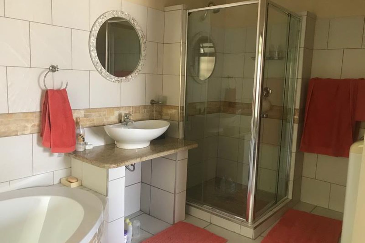 A functional bathroom featuring a corner glass shower enclosure, a vessel sink set on a stone vanity, and a built-in bathtub with tiled surround.