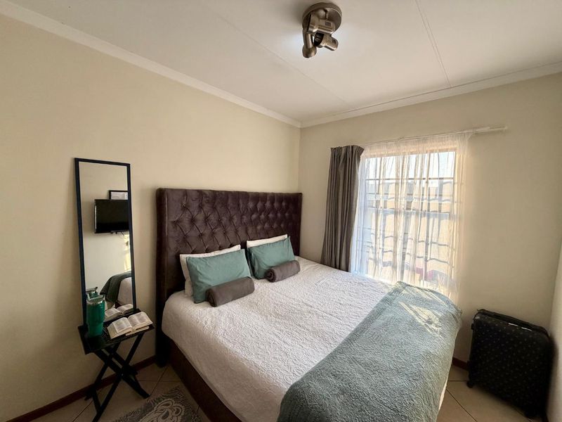 A functional bedroom featuring tiled flooring, neutral wall finishes, and a window with curtain tracks, providing a comfortable and well-lit sleeping space.