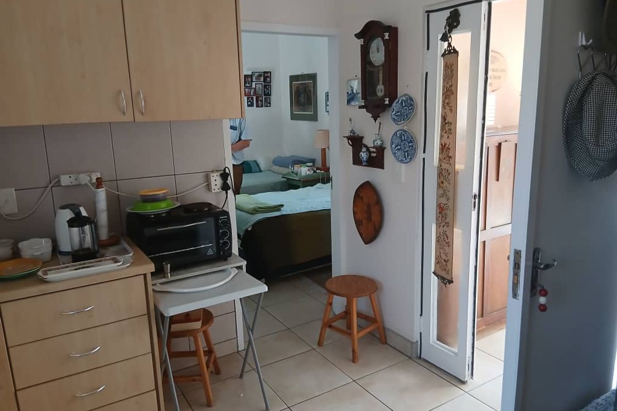 A compact kitchen area featuring light wood-toned cabinetry and tiled flooring, with a direct view into an adjacent bedroom space.