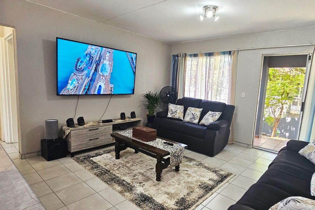 A comfortable living room featuring tiled flooring, neutral walls, and a sliding glass door providing access to an outdoor patio area.