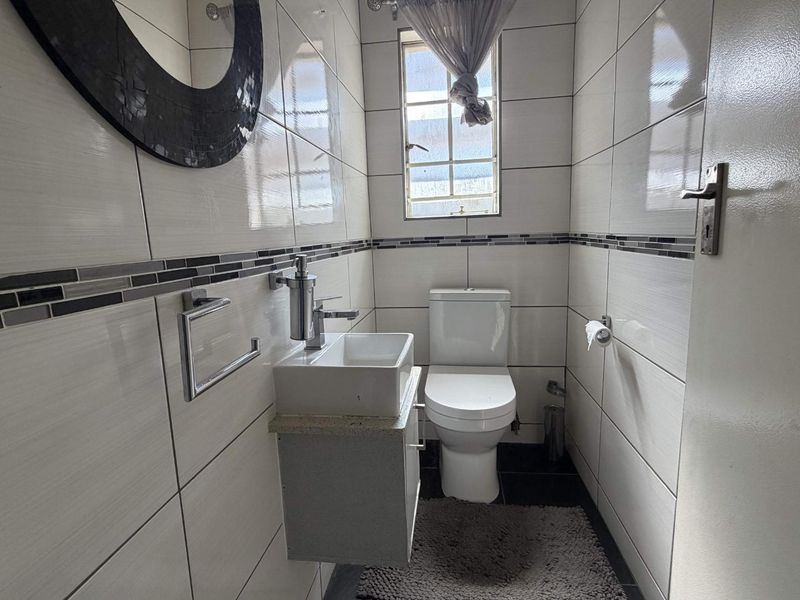 A compact, modern guest bathroom featuring tiled walls, a wall-mounted vanity with a ceramic basin, and a standard toilet.