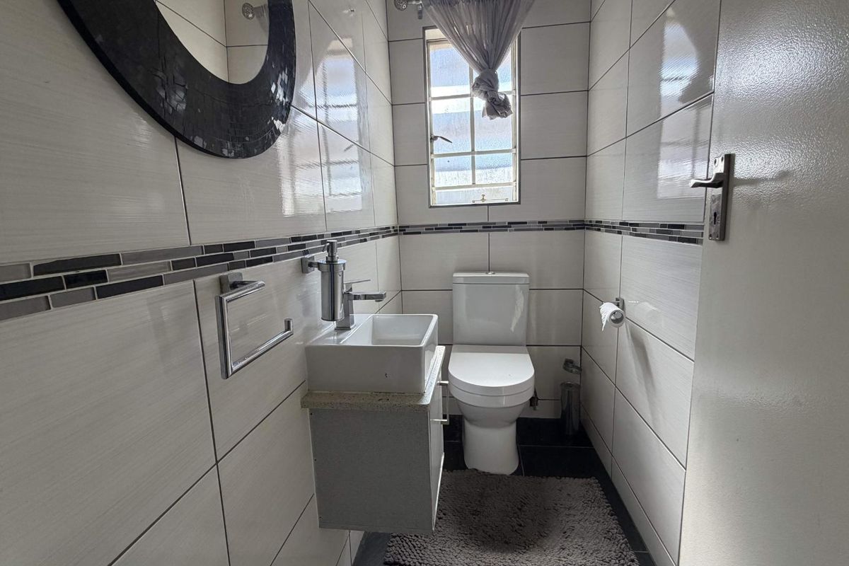 A compact, modern guest bathroom featuring tiled walls, a wall-mounted vanity with a ceramic basin, and a standard toilet.