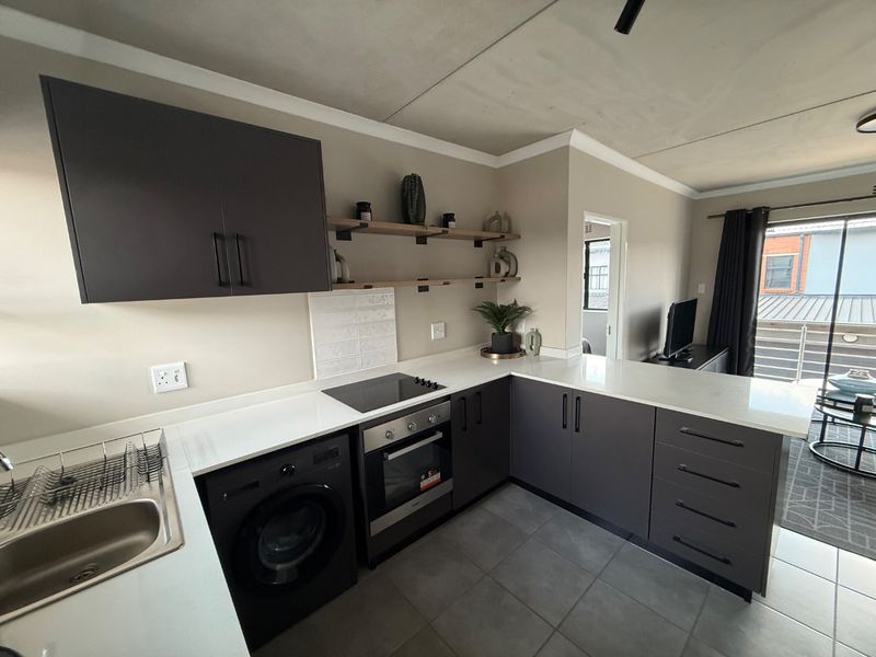 Modern open-plan kitchen featuring dark cabinetry, quartz countertops, integrated appliances, and tiled flooring, seamlessly flowing into the adjacent living area.