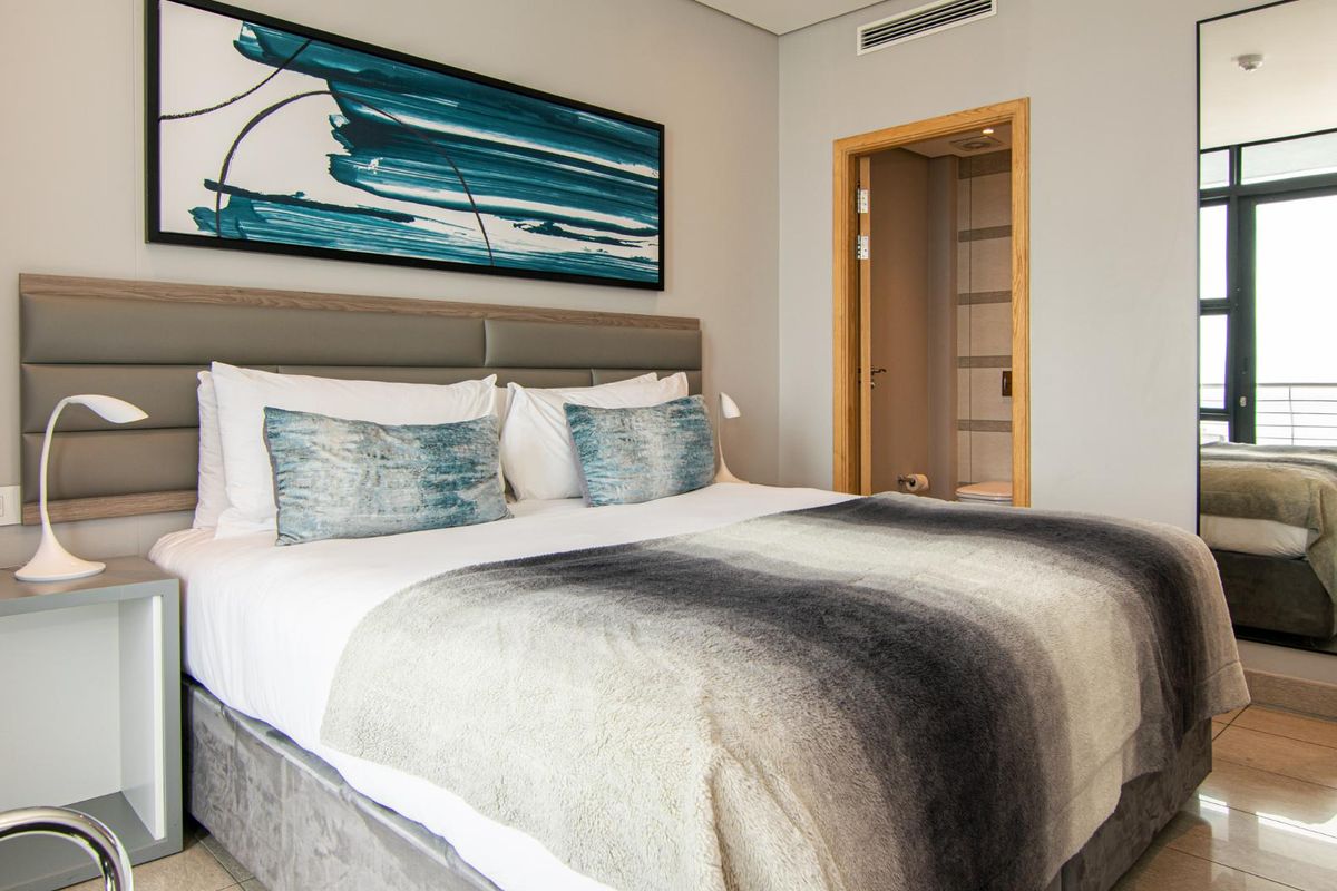 A well-appointed bedroom featuring a neutral color palette, integrated air conditioning vent, and an en-suite bathroom entrance.