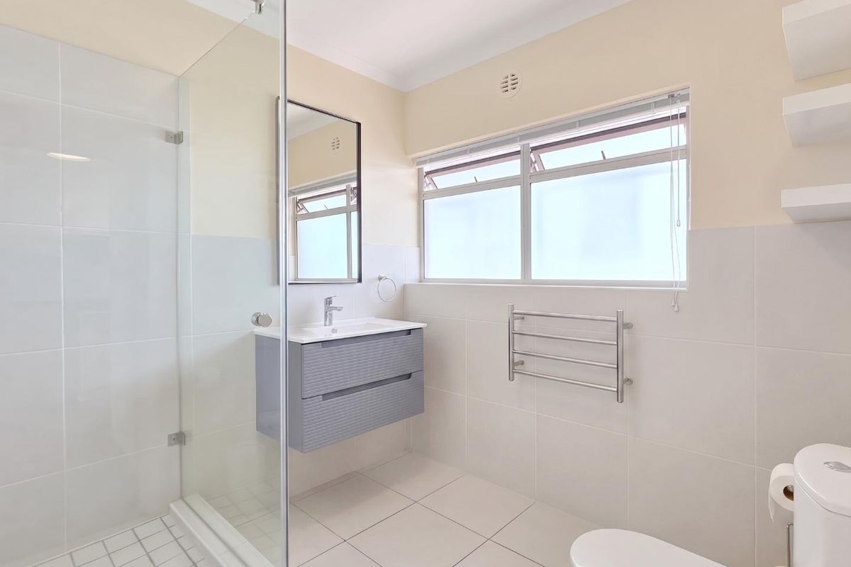 A clean, modern bathroom featuring a glass-enclosed shower, wall-mounted vanity, heated towel rail, and neutral tiled finishes throughout.