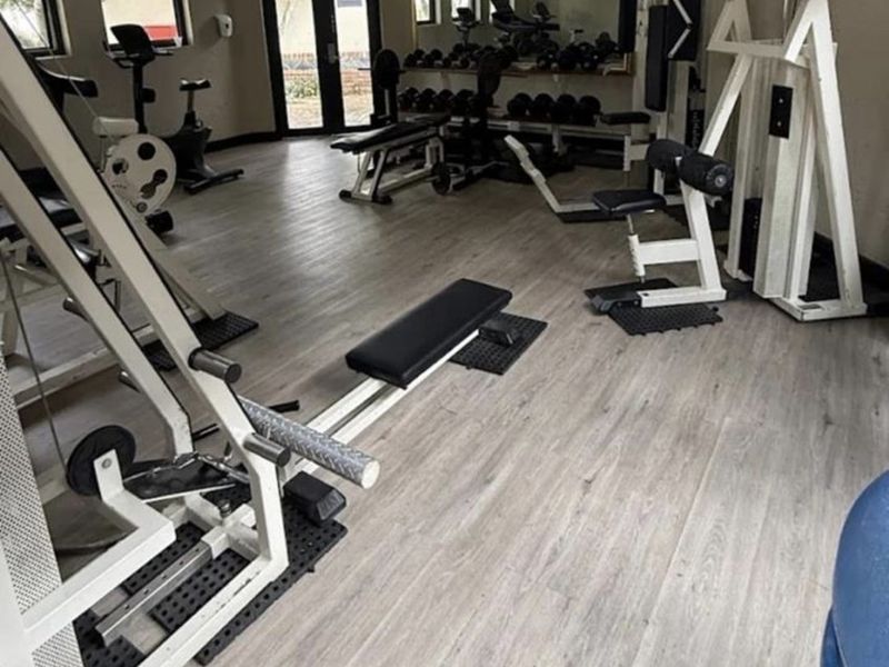 A well-equipped residential gym featuring laminate flooring, recessed lighting, and a large wall-mounted mirror, providing a functional space for fitness activities.