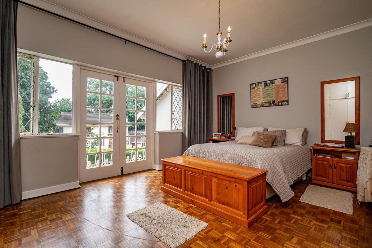 Spacious bedroom featuring classic parquet flooring, a chandelier, and double doors opening to an outdoor area, providing ample natural light.