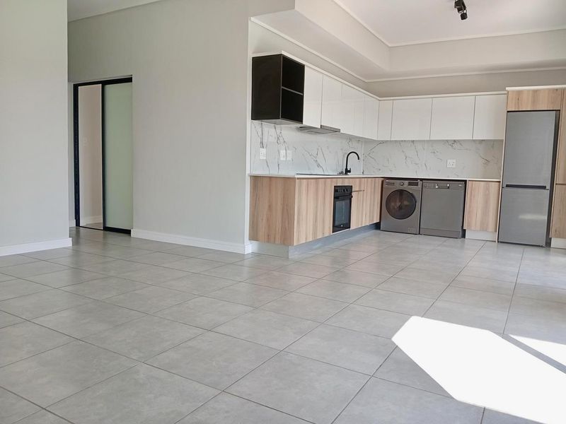 Modern open-plan kitchen featuring sleek white and wood-grain cabinetry, marble-look splashback, and large format floor tiles in a bright, spacious living area.