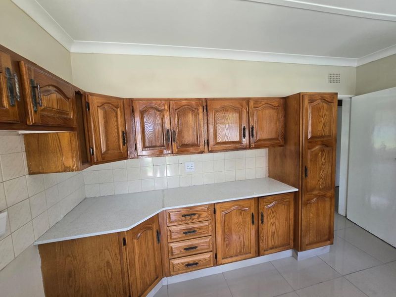 A functional kitchen featuring traditional wooden cabinetry, light-colored laminate countertops, a tiled backsplash, and neutral floor tiles.