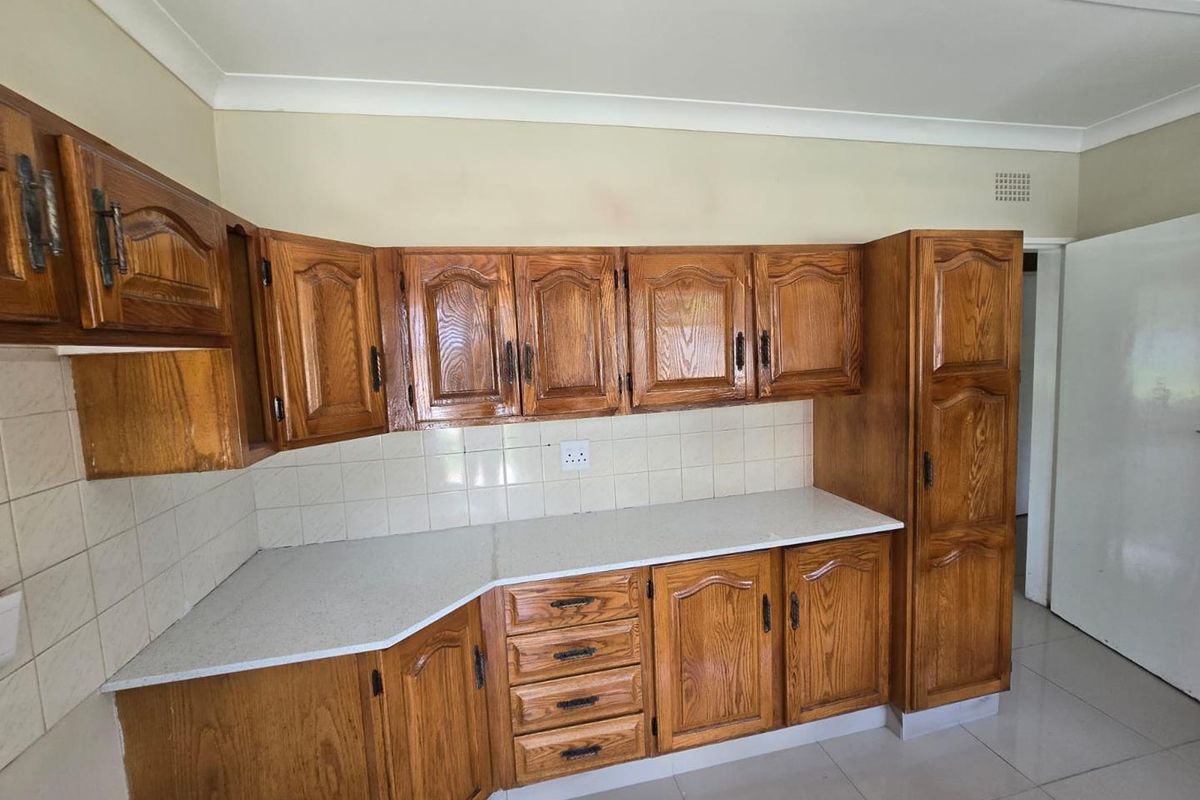 A functional kitchen featuring traditional wooden cabinetry, light-colored laminate countertops, a tiled backsplash, and neutral floor tiles.