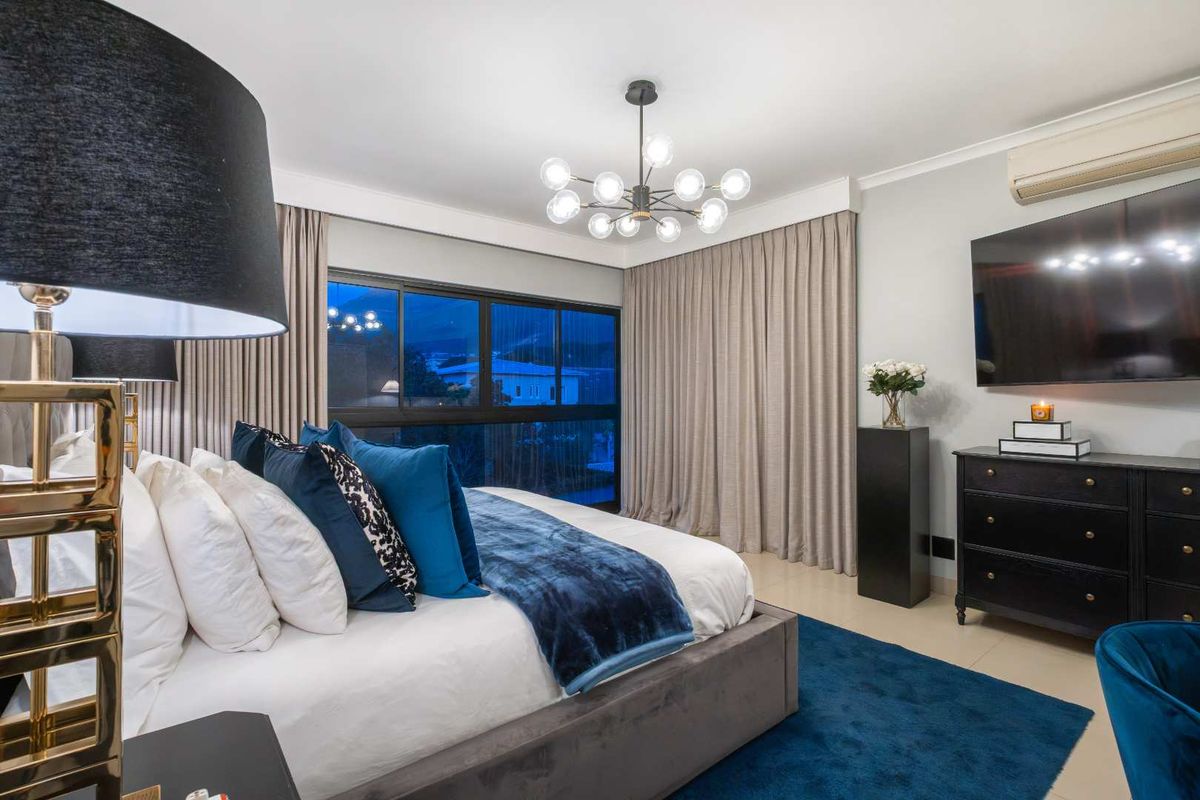 A well-appointed bedroom featuring modern tiled flooring, a contemporary chandelier, and a sliding glass door with integrated curtain tracks.