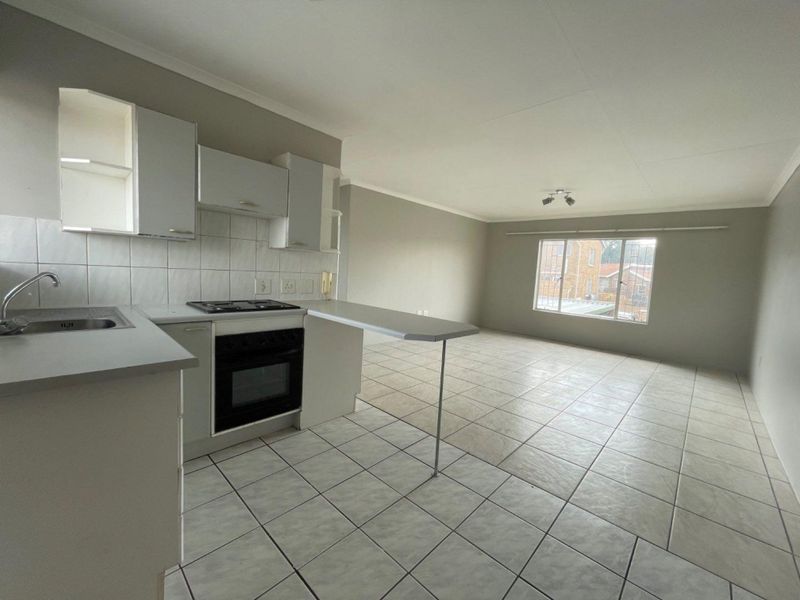 An open-plan kitchen and living area featuring tiled flooring, built-in cabinetry, a breakfast bar, and a large window providing natural light.