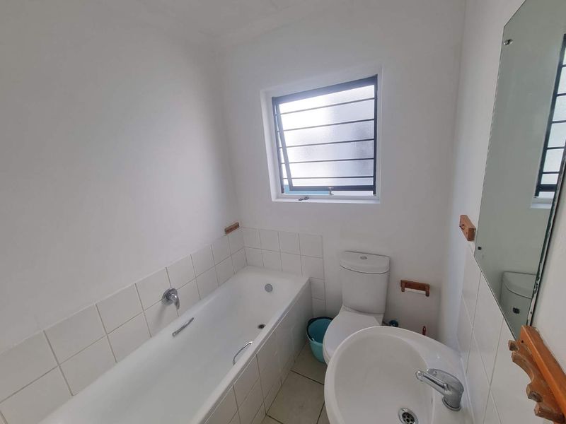 A functional bathroom featuring a bathtub, pedestal basin, and toilet with white tiled splashbacks and a louver window for ventilation.