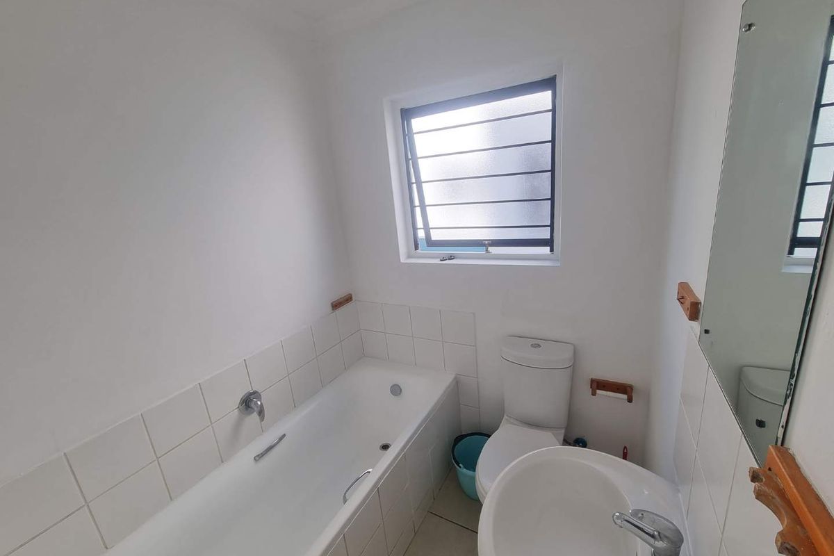 A functional bathroom featuring a bathtub, pedestal basin, and toilet with white tiled splashbacks and a louver window for ventilation.