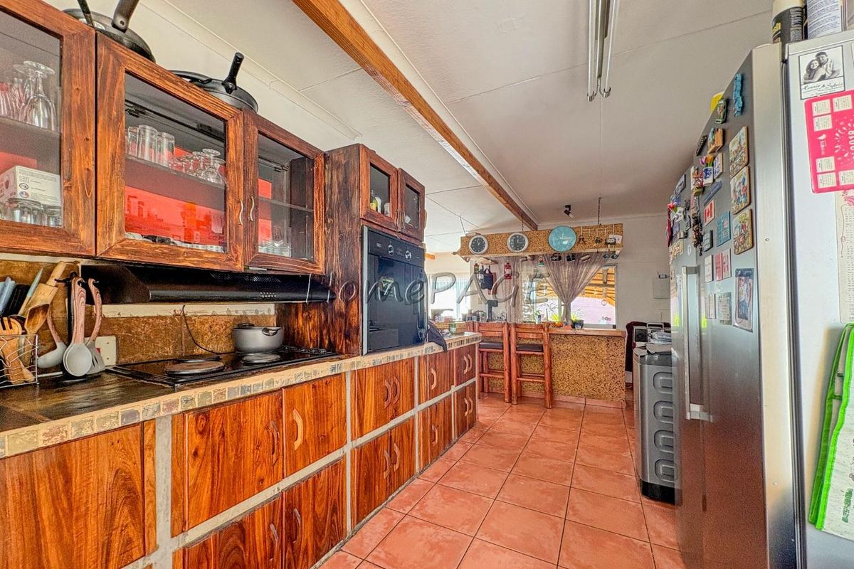 A rustic kitchen featuring dark wood cabinetry, integrated oven, hob, and a breakfast bar area with tiled flooring.